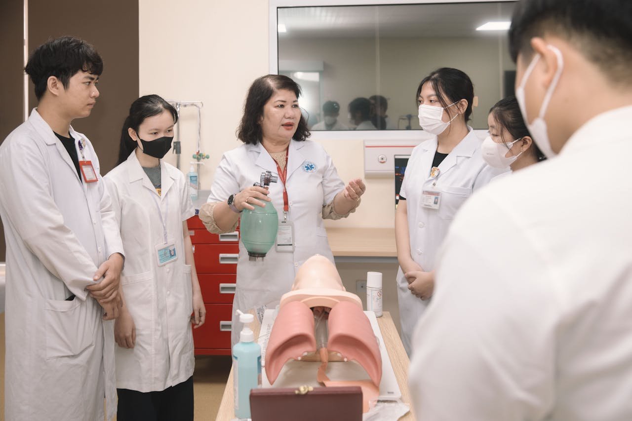 Group of medical students practicing skills with a training mannequin in a classroom setting.